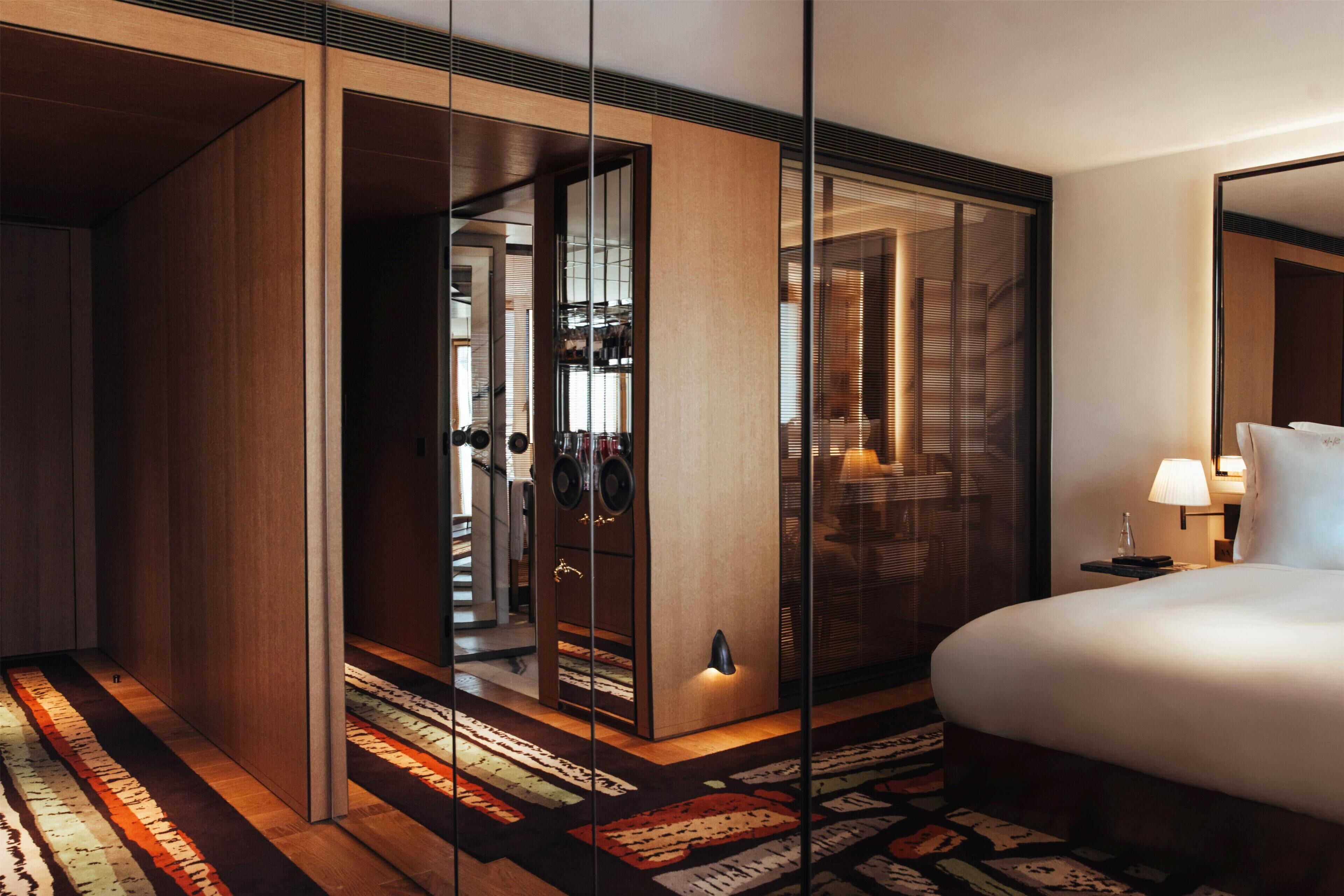 Habitación de hotel con cama, mesita de noche, lámpara, espejo, armario y alfombra.