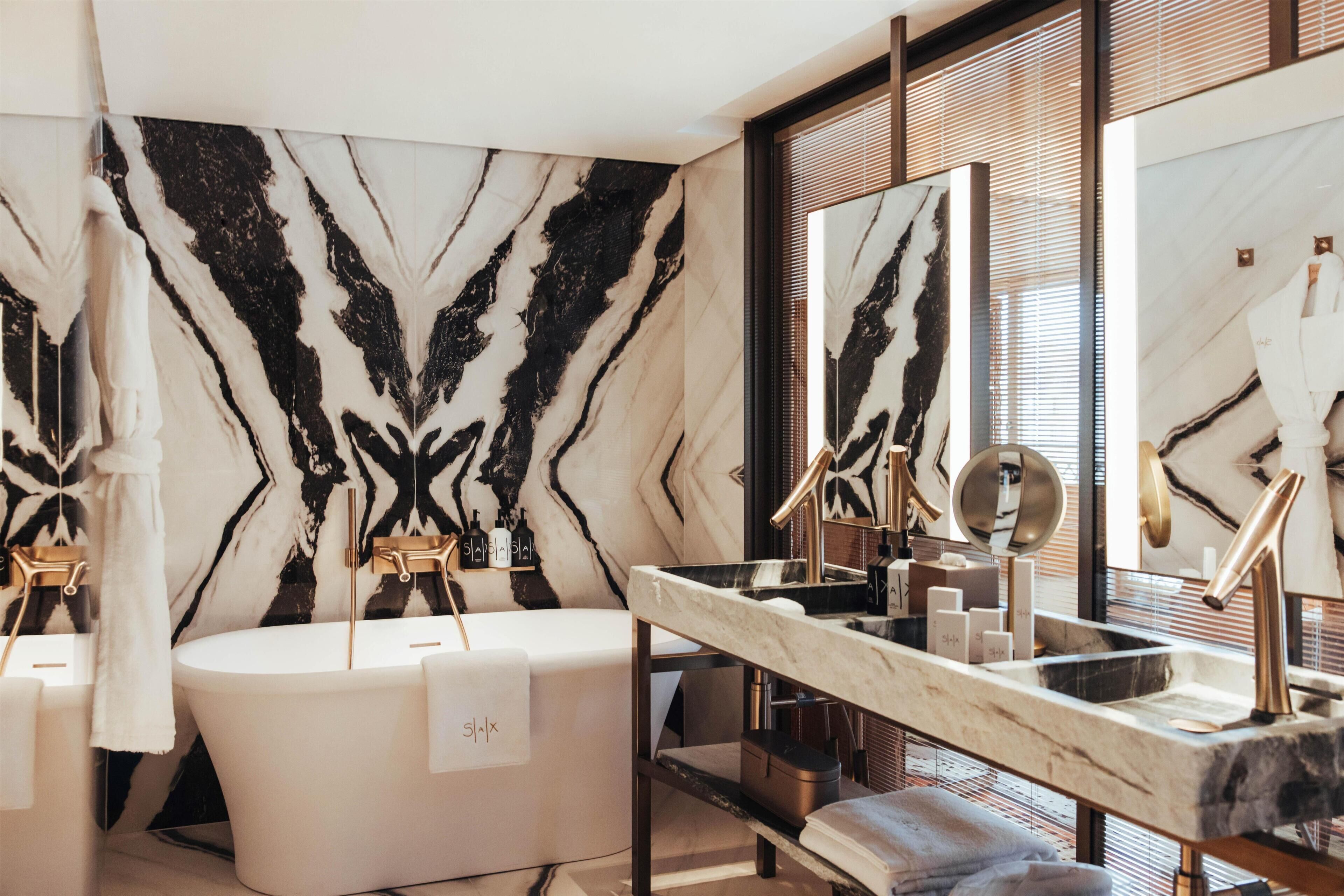A modern bathroom with a freestanding bathtub, a large mirror, and a marble wall.