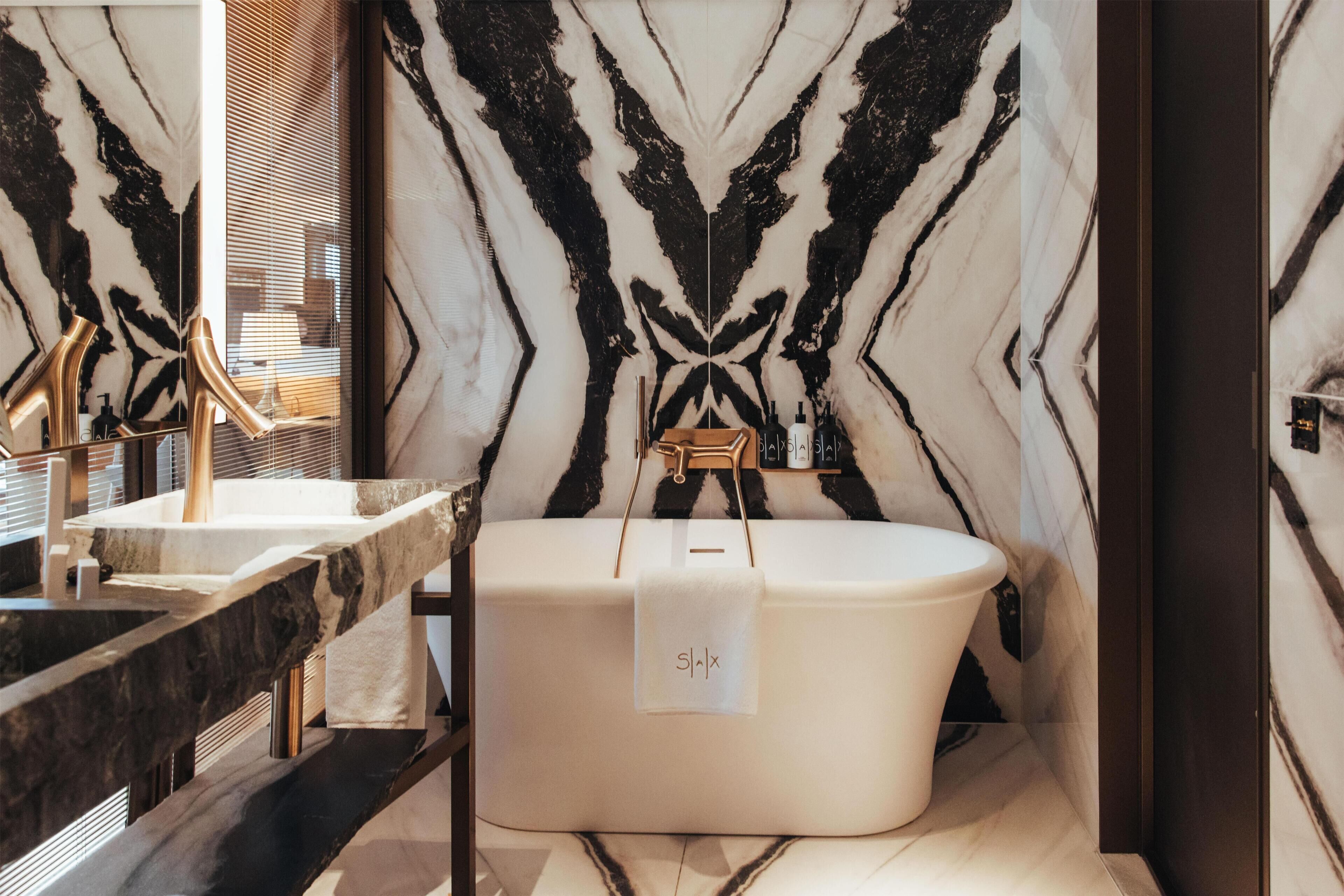 A modern bathroom with a marble wall, a freestanding bathtub, and a vanity with a mirror.