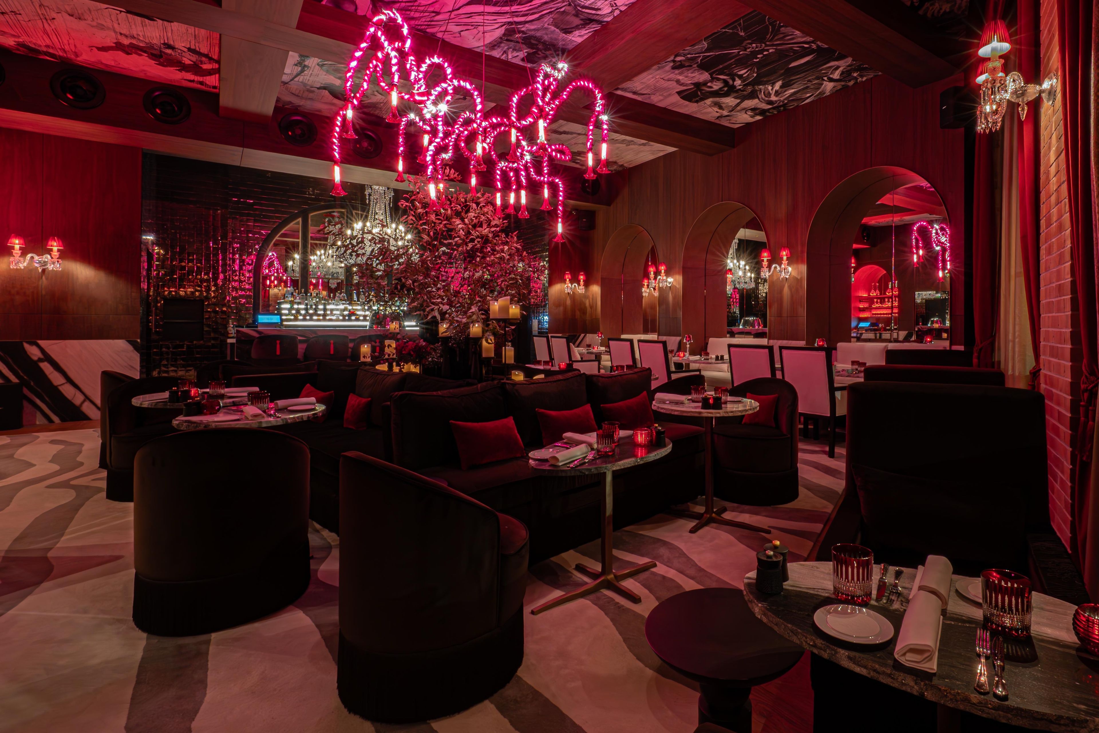 Een zwak verlicht restaurant met rode sfeerverlichting, meerdere zithoeken en een bar.