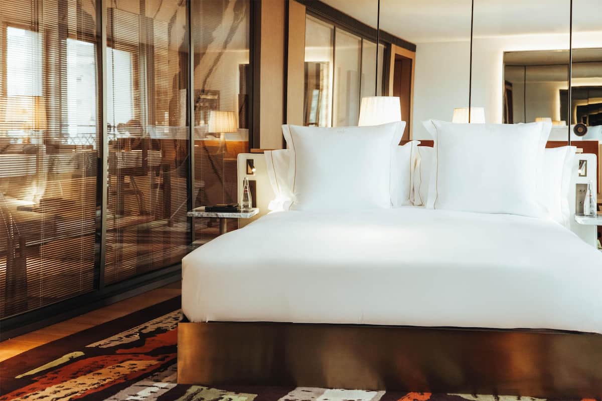 Hotellihuone, jossa on suuri sänky, lasiseinä ja näkymä ulos.