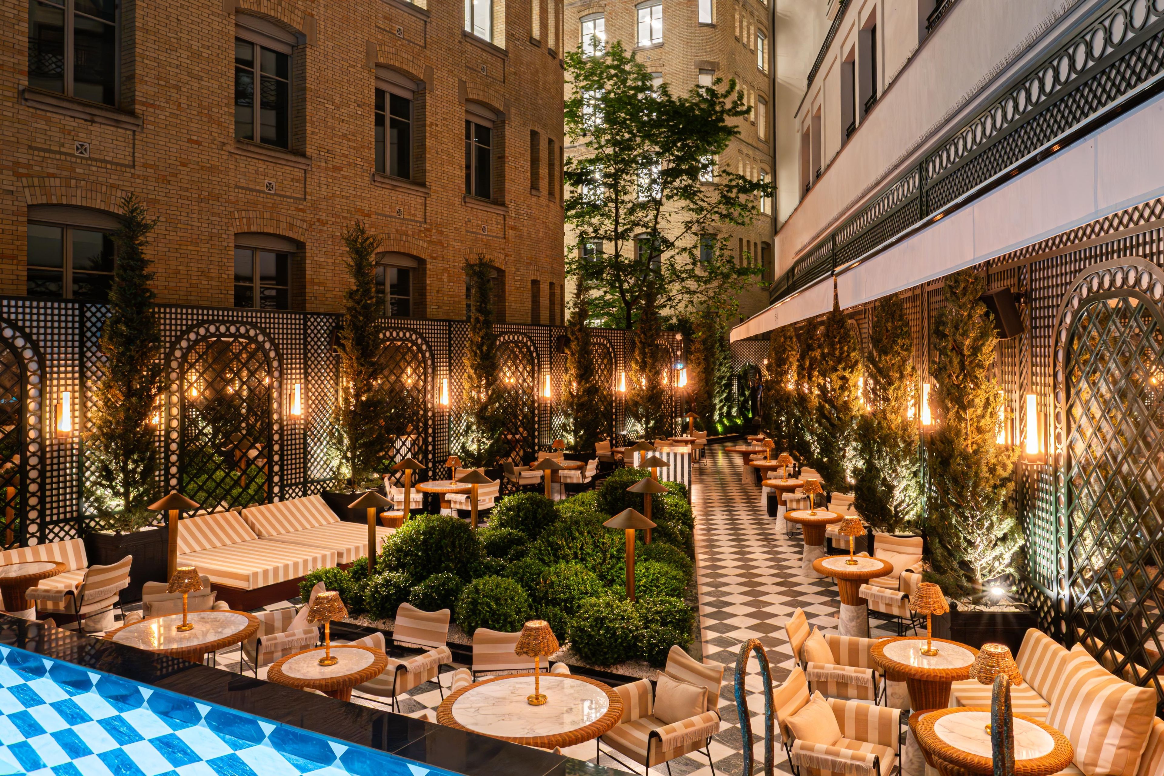A rooftop bar with outdoor seating, a pool, and a view of the cityscape.