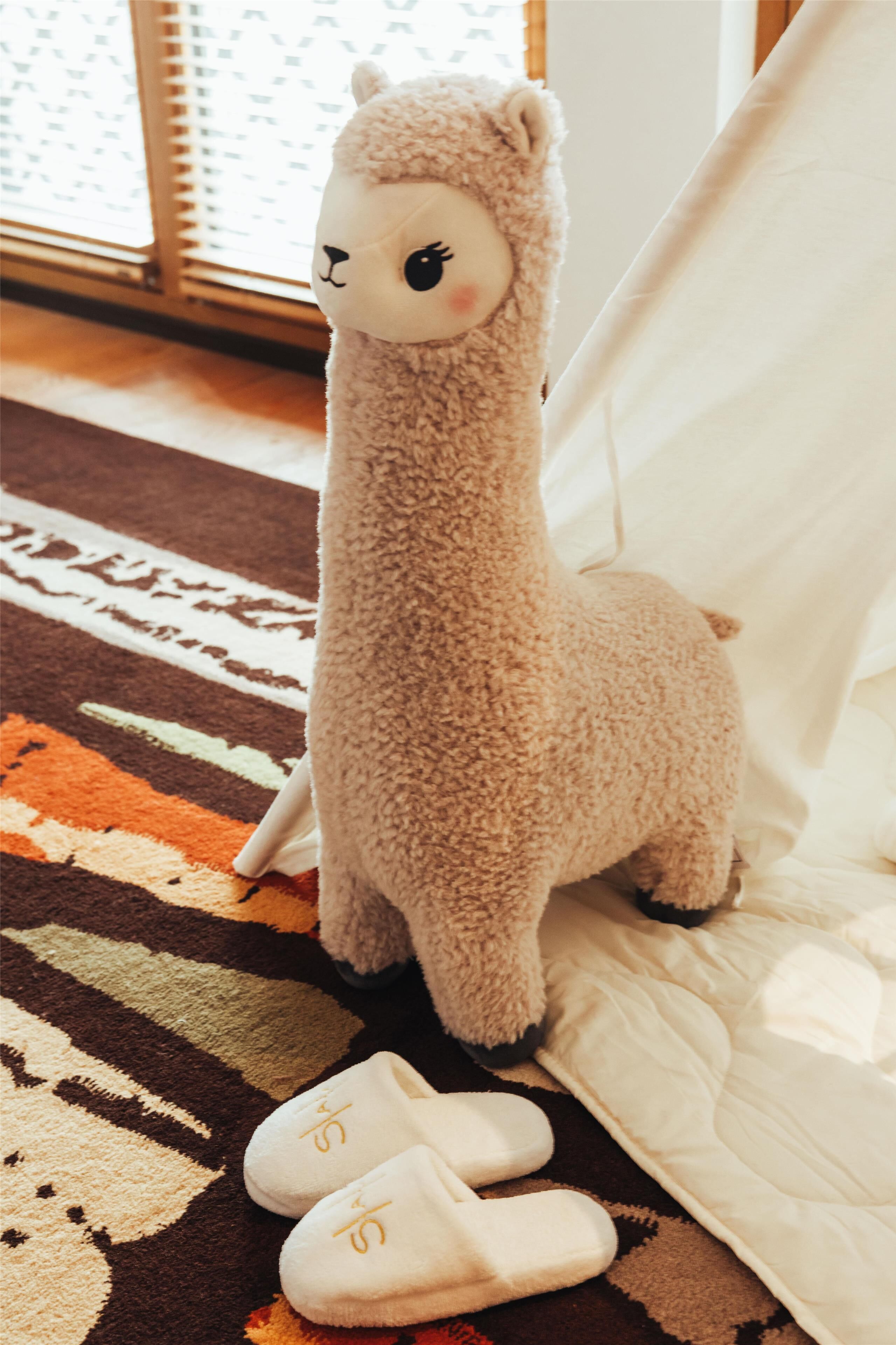 Un peluche de llama, un par de pantuflas y una alfombra estampada en una habitación con una estructura parecida a una tienda de campaña.