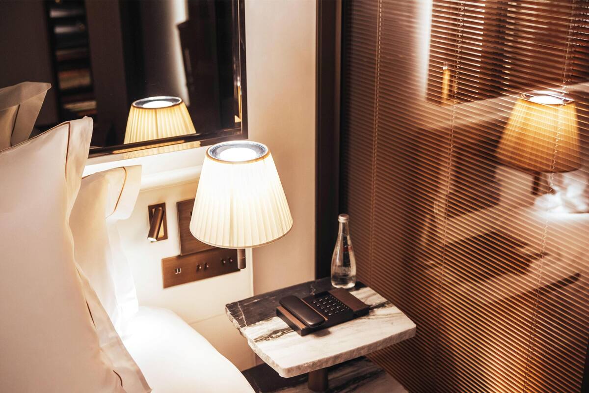 Hotellihuone, jossa on sänky, yöpöytälamput, yöpöytä, jossa on puhelin, vesipullo ja peili.