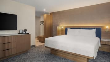 A modern hotel room with a large bed, a wooden dresser, a flat-screen TV, and a patterned rug.