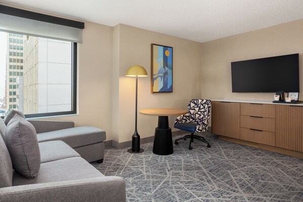 Une chambre d’hôtel moderne, équipée d’un canapé, d’une petite table ronde, d’une lampe, d’un téléviseur et d’un tapis à motifs.