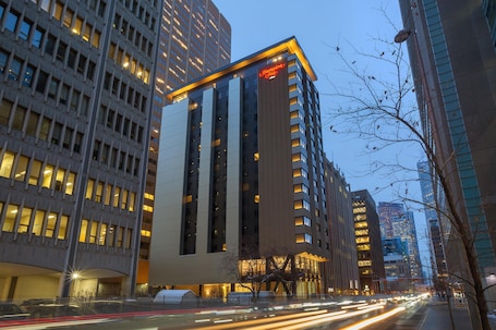A modern hotel with a prominent vertical design, large windows, and a visible sign for Hampton Inn.