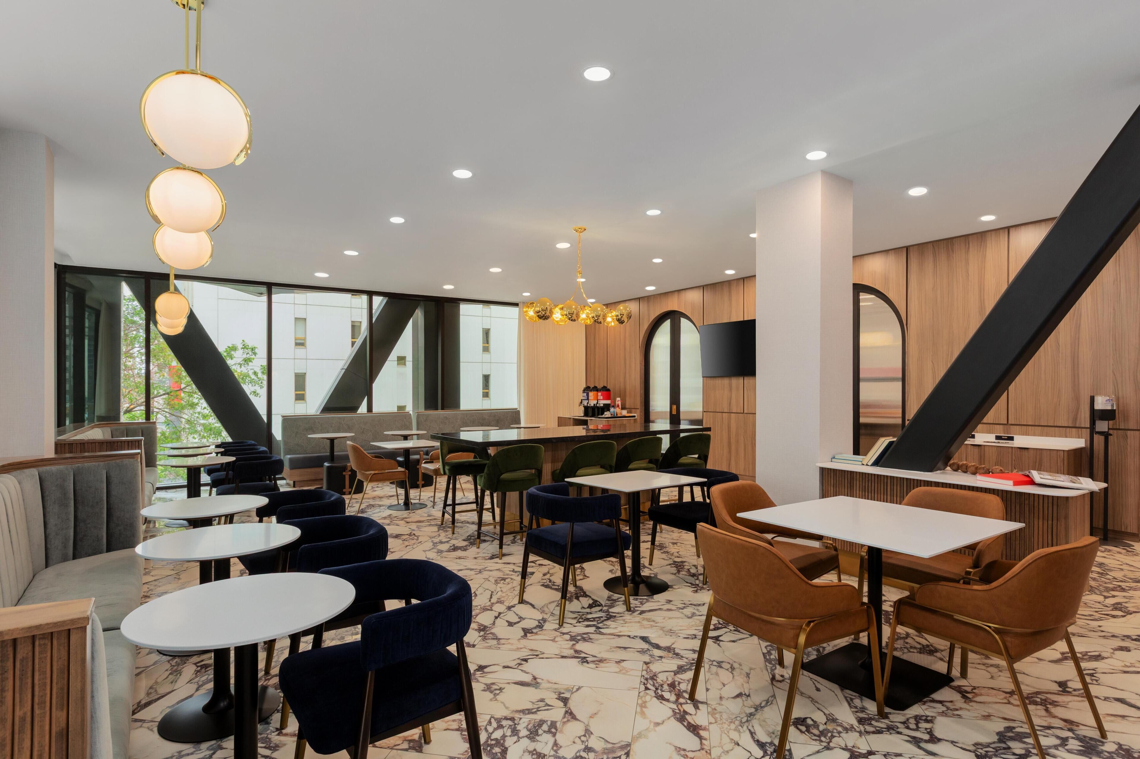 Un restaurante moderno con suelos de mármol, diversas opciones de asientos que incluyen mesas redondas y cabinas, y una variedad de sillas.