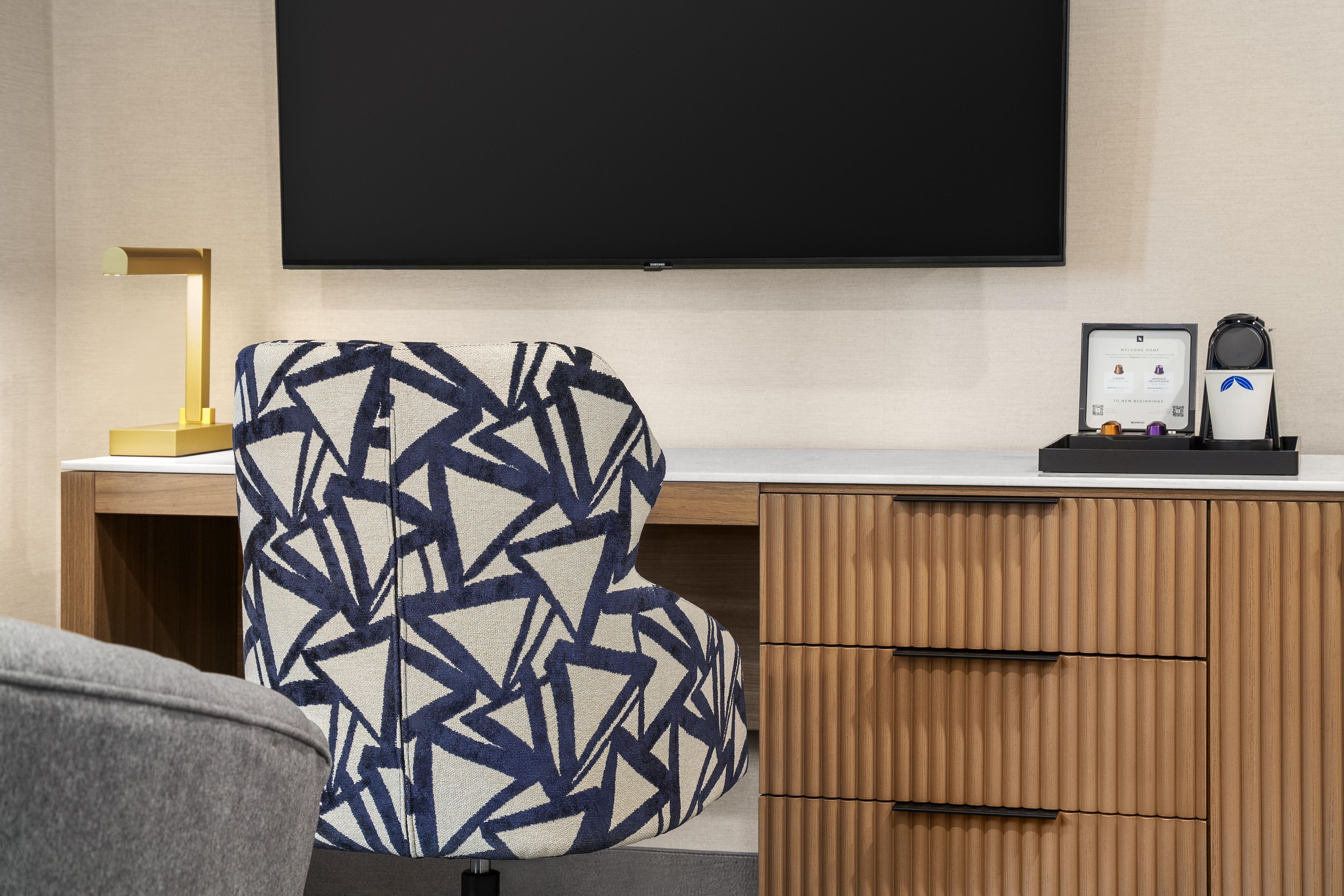 Habitación de hotel con una silla moderna, un escritorio, un televisor de pantalla plana y un minibar.