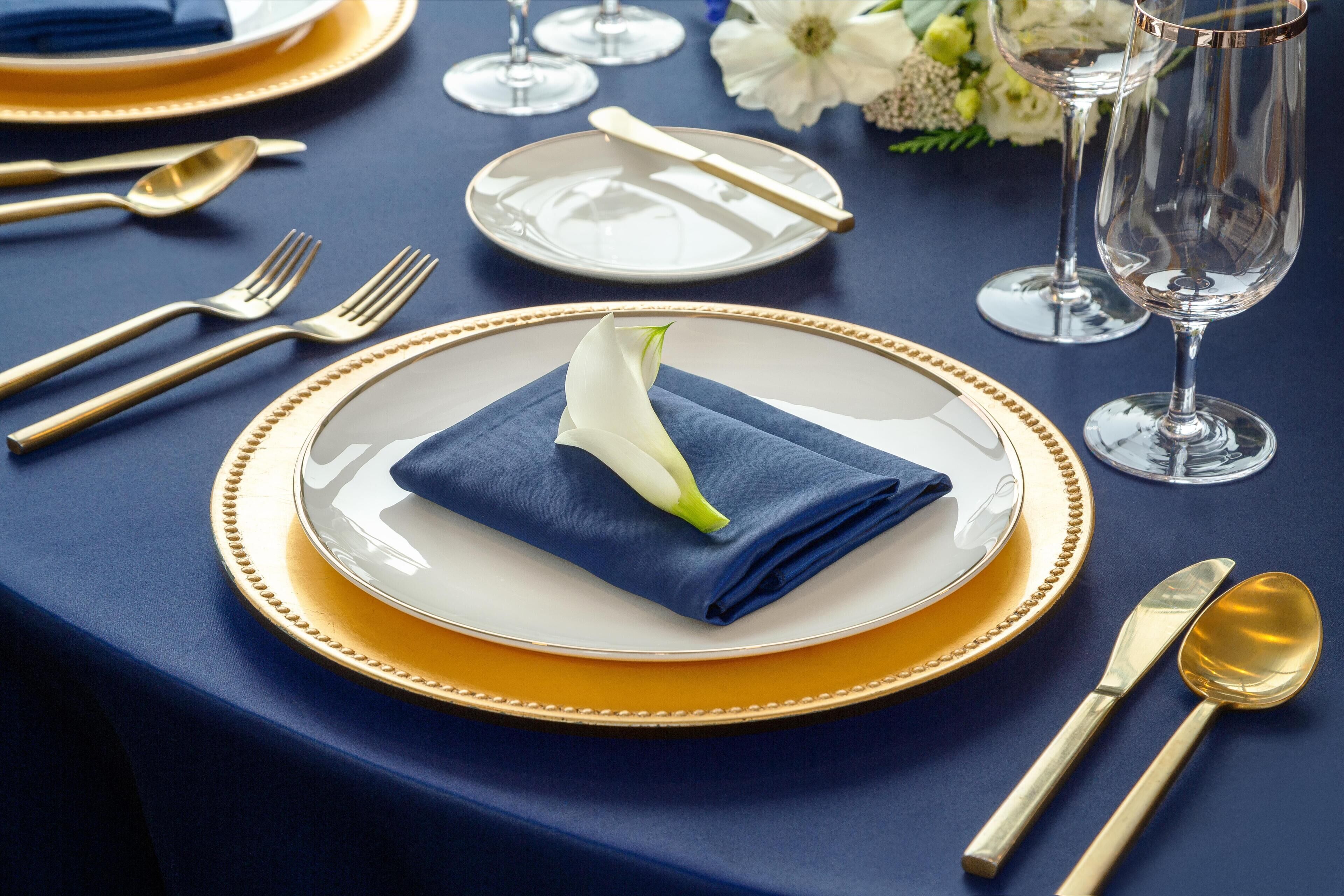 A table set with gold and white dinnerware, including plates, cutlery, and glasses, arranged on a blue tablecloth.
