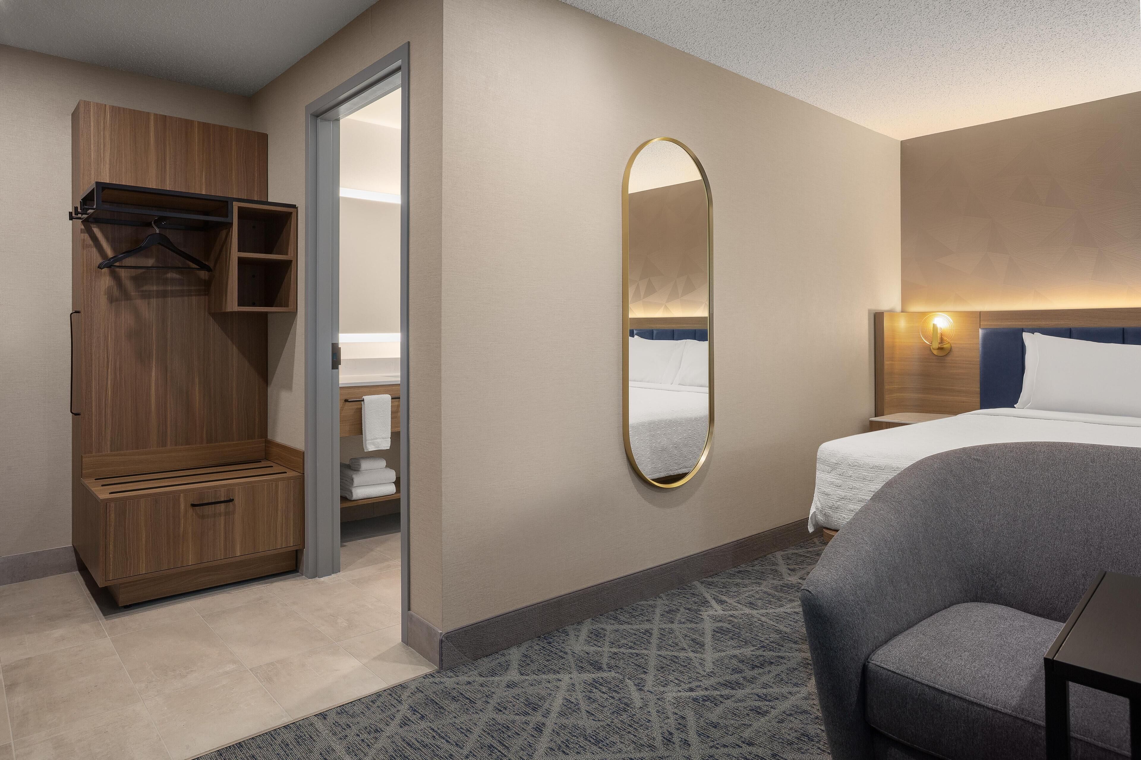 A hotel room with a bed, a seating area, a wardrobe, and a bathroom visible through an open door.