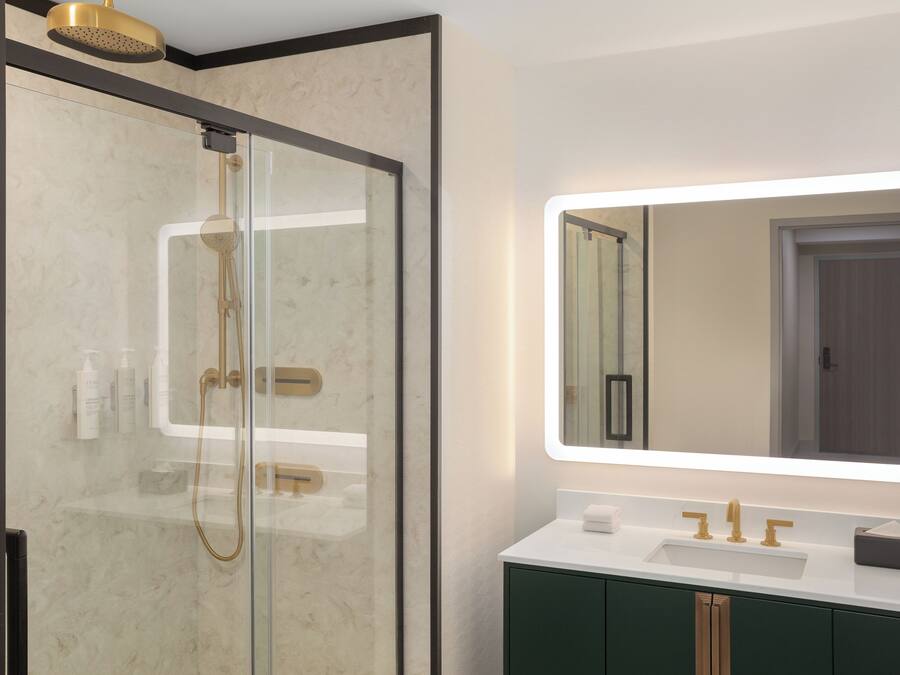 A modern bathroom with a glass-enclosed shower, a white sink with gold fixtures, and a large mirror with integrated lighting.