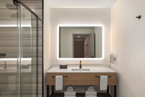 Une salle de bain moderne dotée d’une douche à parois de verre, d’un meuble-lavabo en bois avec un vasque blanche et d’un grand miroir avec éclairage intégré.