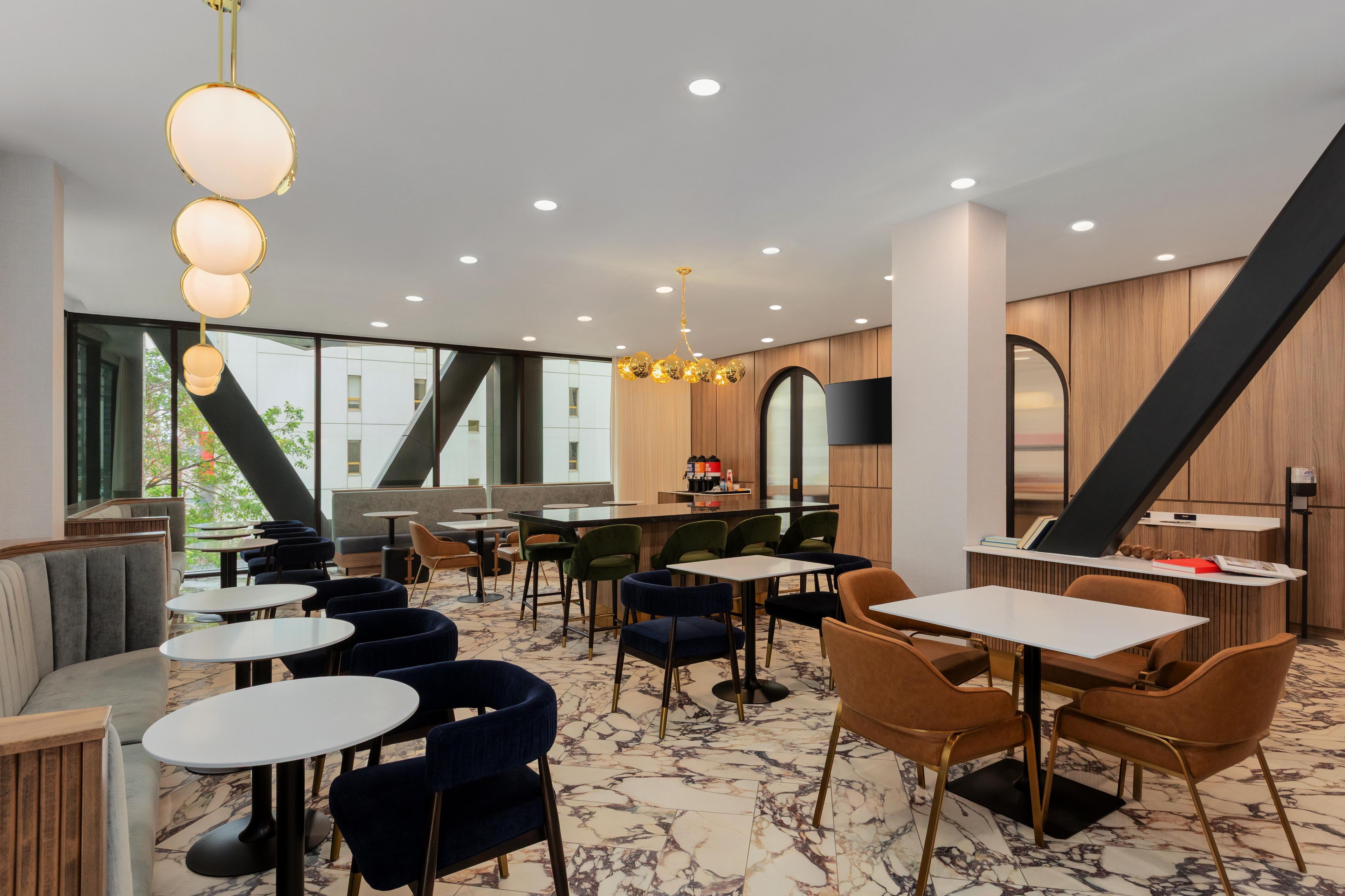 A modern restaurant interior with marble flooring, multiple seating arrangements including round tables and booths, and a variety of chairs.