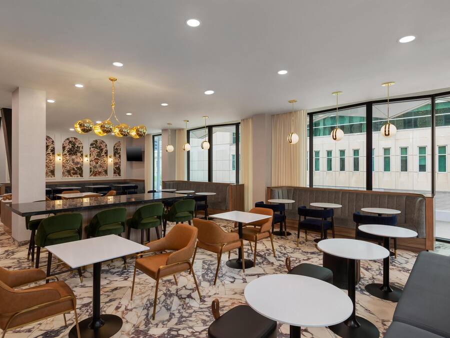 A modern restaurant with marble flooring, green and brown chairs, round tables, and a bar area with artwork on the wall.