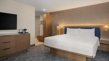 Habitación de hotel moderna con una cama grande, cabecero de madera, mesitas de noche, un televisor de pantalla plana y un armario empotrado.