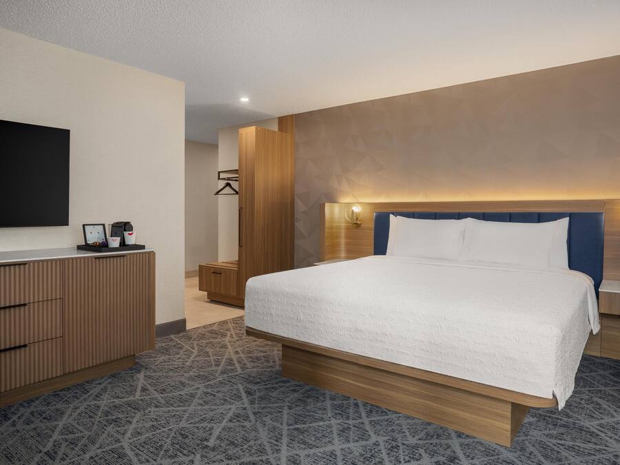 Habitación de hotel moderna con una cama grande, cabecero de madera, mesitas de noche, un televisor de pantalla plana y un armario empotrado.