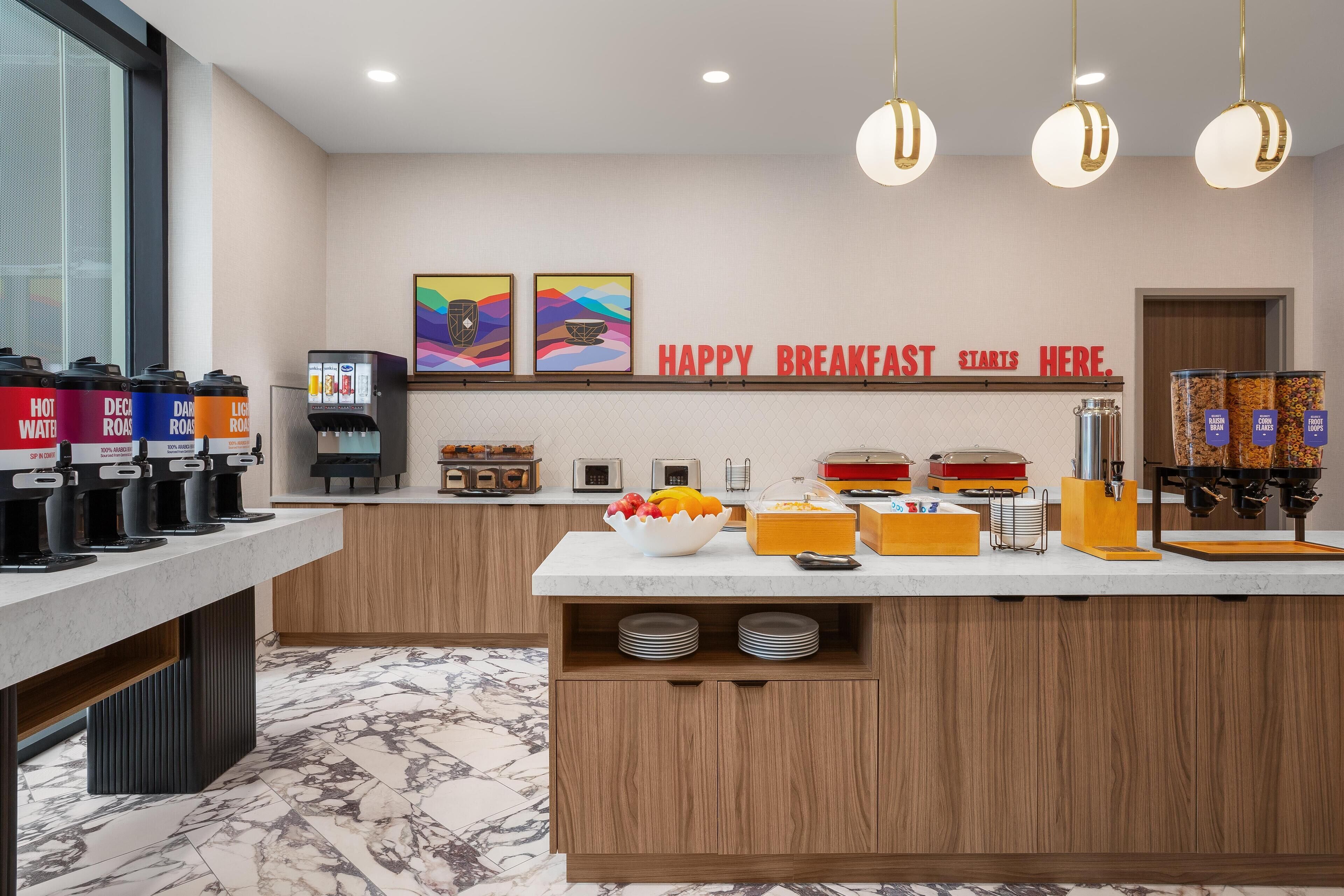 Una barra de desayuno con dispensadores de café, un frutero y un cartel que dice "HAPPY BREAKFAST STARTS HERE".