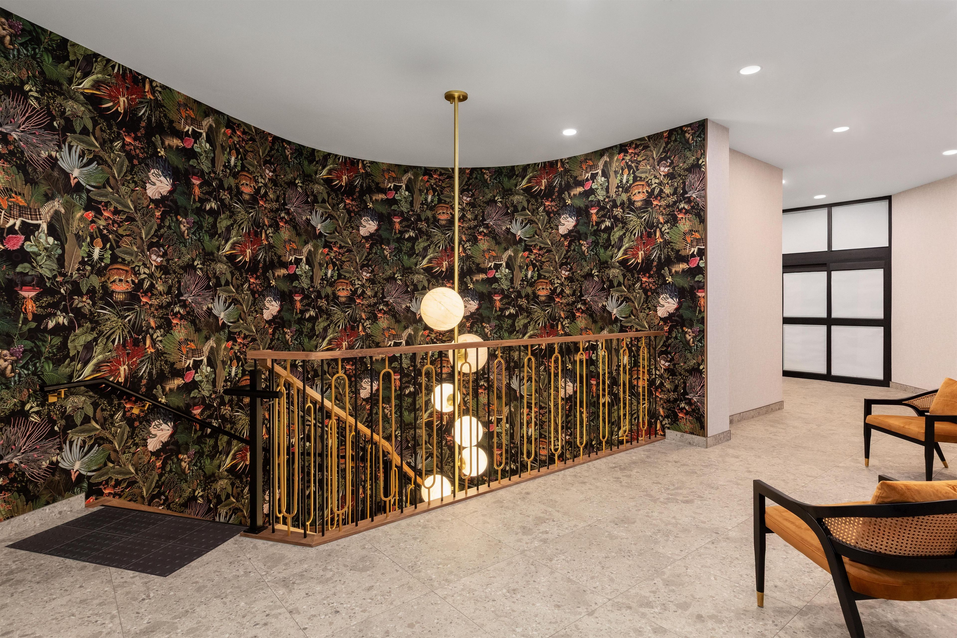 Un interior moderno con una pared curva decorada con un papel tapiz floral denso, una barandilla dorada y una lámpara contemporánea.