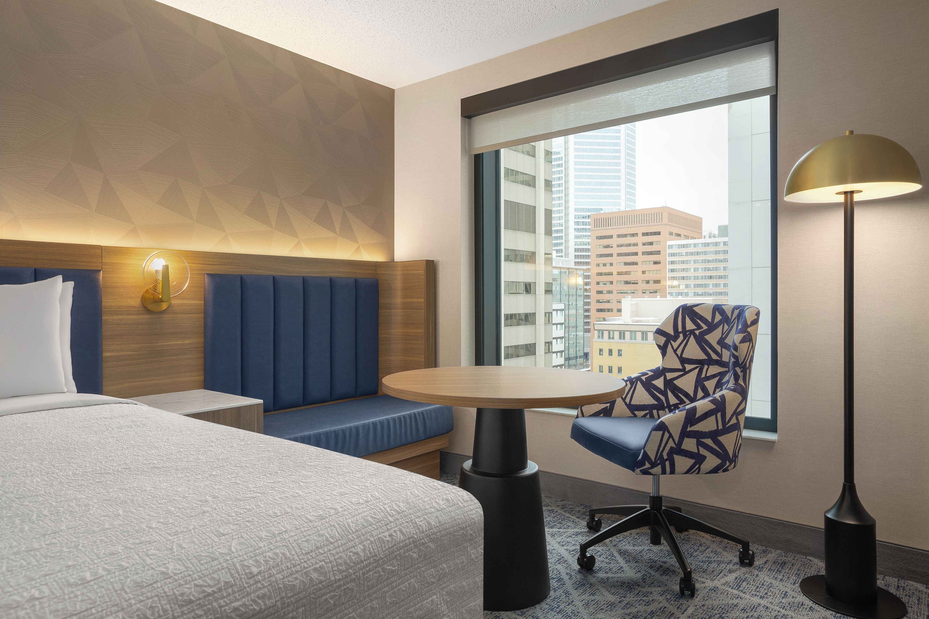 A hotel room with a bed, a seating area, a table, and a lamp.