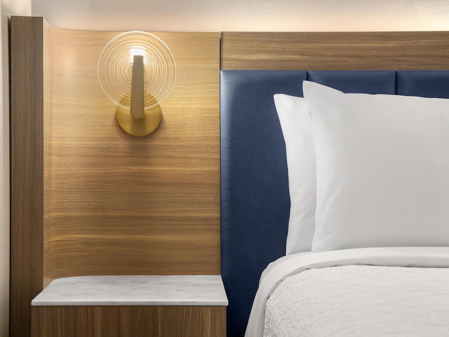A neatly made bed with white linens, a wooden headboard, and a bedside table with a lamp.