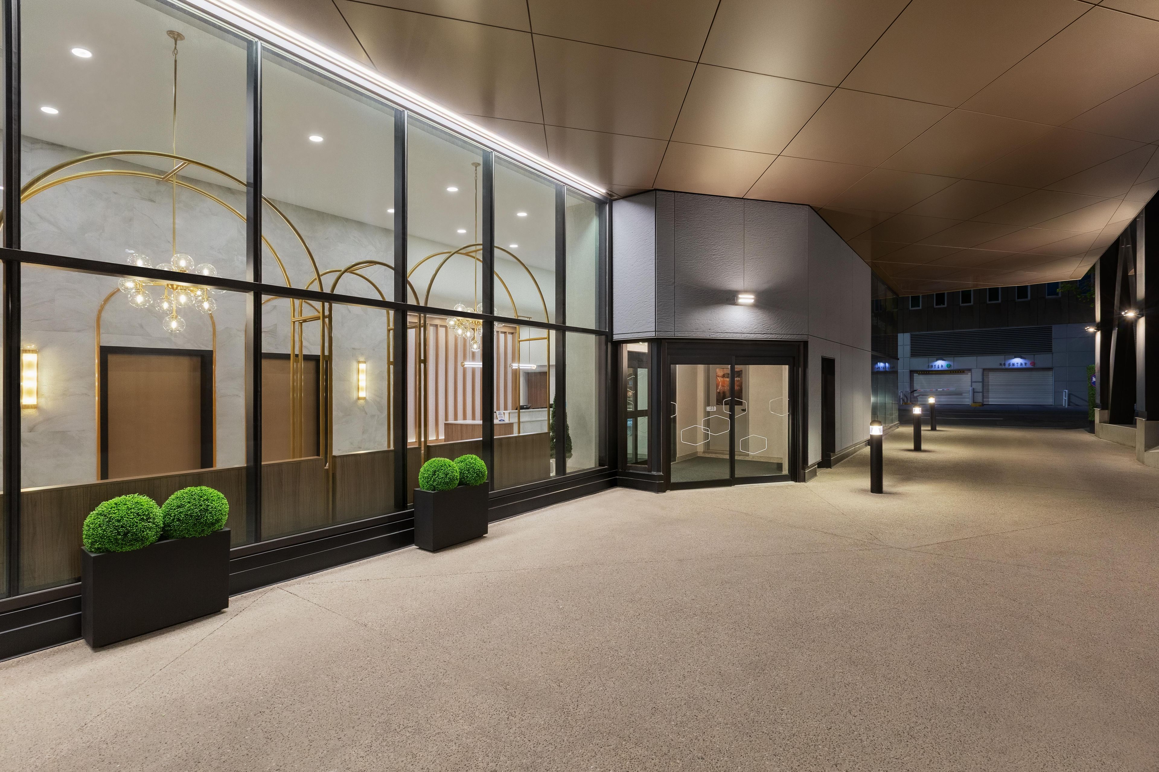 Un hall d’hôtel moderne avec des portes vitrées, un comptoir d’accueil et un espace détente agrémenté de plantes.