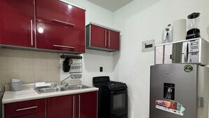 A kitchen with red cabinets, a stainless steel refrigerator, a stove, and a sink.