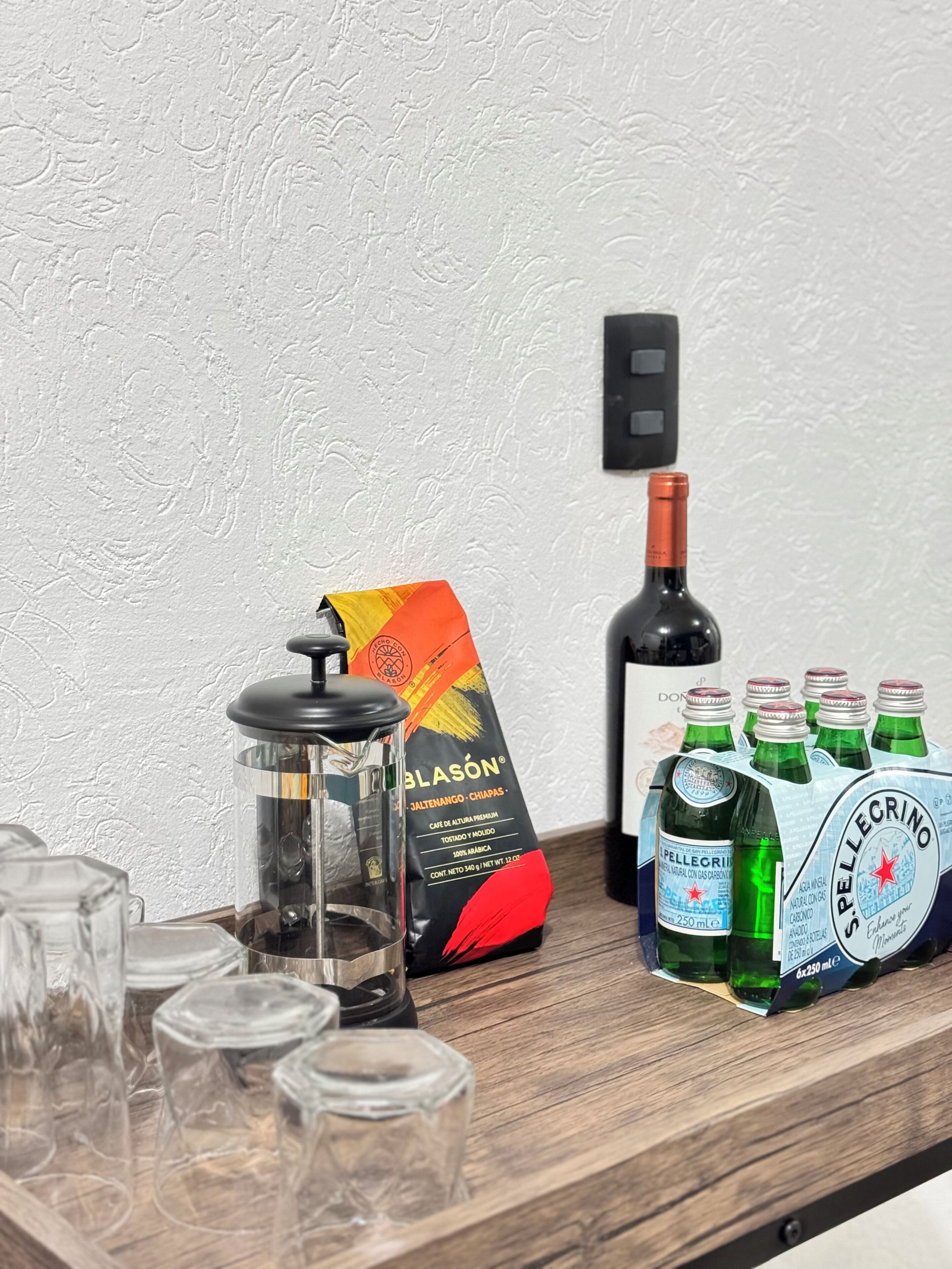 A wooden table with a coffee grinder, a bottle of wine, and a pack of Pellegrino water bottles.