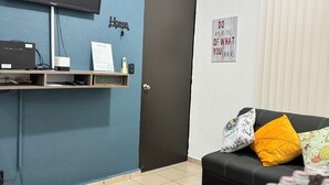 A living room with a TV, a shelf with electronic devices, a door, and a sign on the wall.