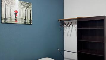 A bedroom with a bed, a wardrobe, a coat rack, and a painting on the wall.
