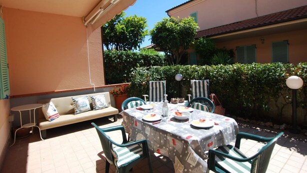Une terrasse extérieure avec une table dressée pour le repas, entourée de chaises et d’un banc.