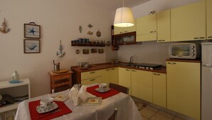 Une cuisine compacte avec des meubles de couleur jaune, un four à micro-ondes et une table à manger dressée avec des assiettes et un set de table rouge.