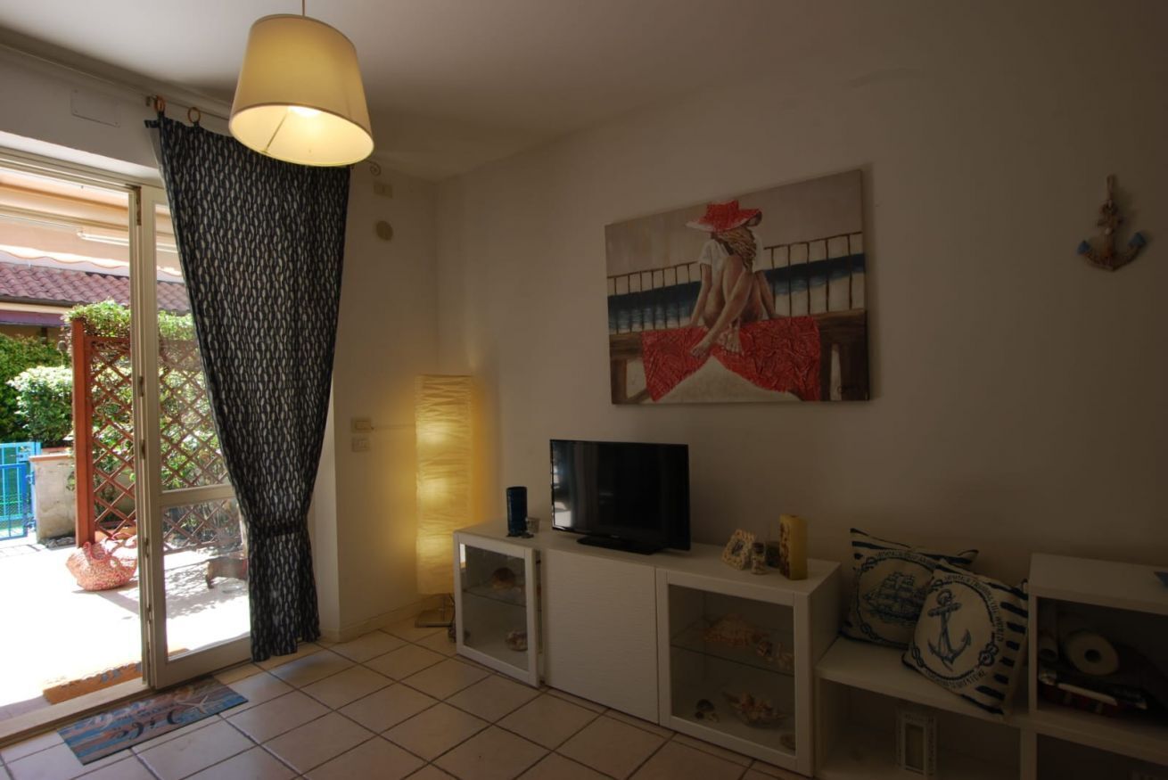 A living room with a TV, a painting, and a sliding glass door leading to an outdoor area.