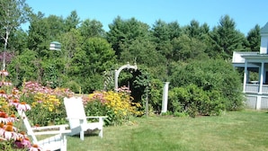 Un jardin avec une chaise blanche, un belvédère et un bâtiment blanc doté d’un balcon.