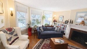 Un salon avec un canapé, un fauteuil et une cheminée. On y trouve également des étagères et une plante en pot.