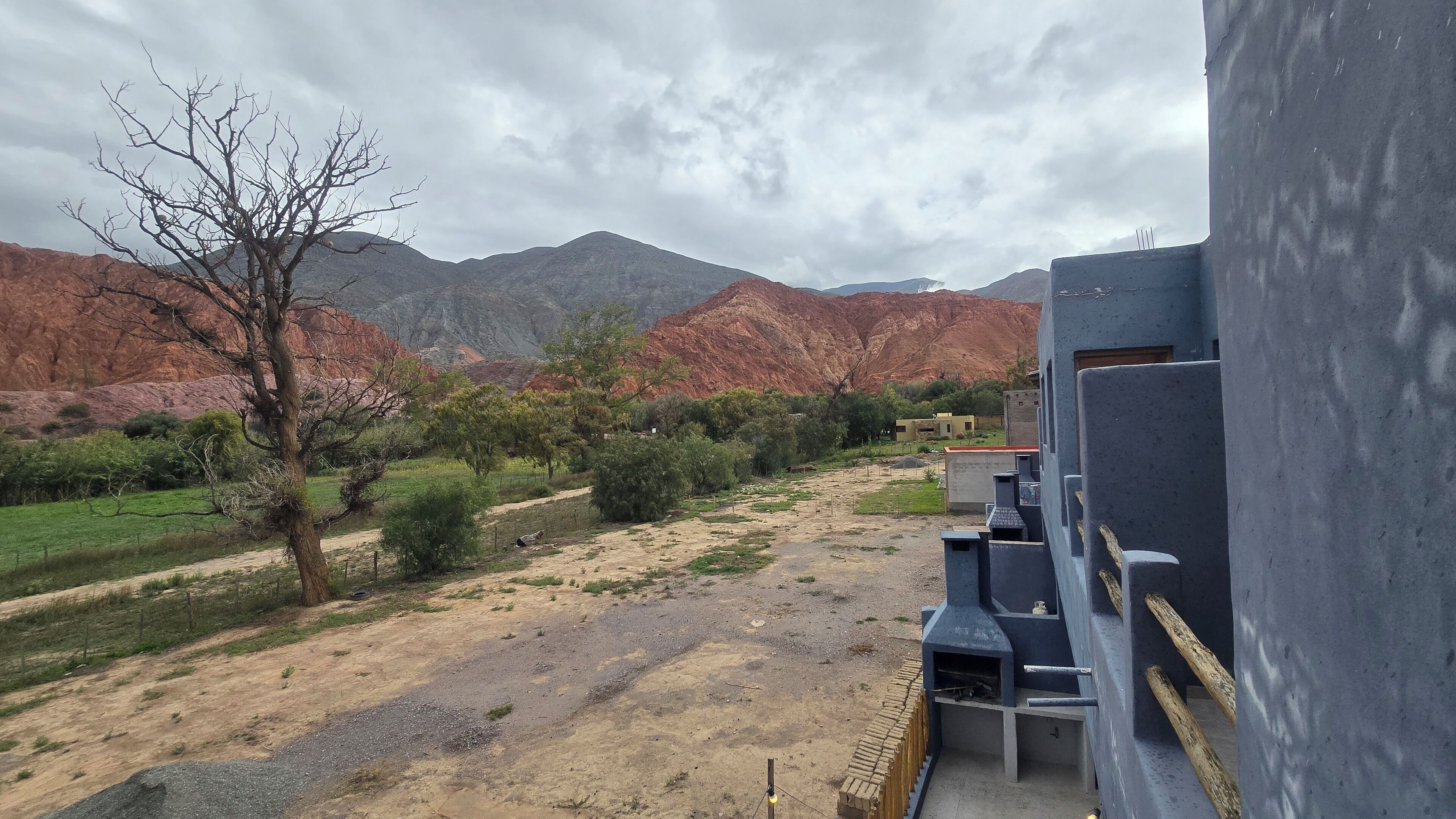 Une vue d’un paysage rural avec des montagnes en arrière-plan, un chemin de terre et un bâtiment doté d’un espace barbecue.