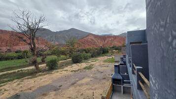 Une vue d’un paysage rural avec des montagnes en arrière-plan, un chemin de terre et un bâtiment doté d’un espace barbecue.