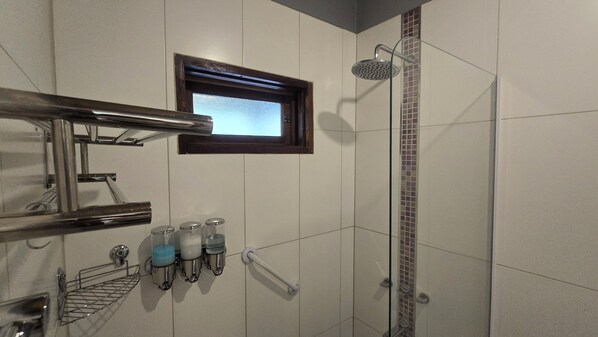 Un espacio de ducha con puerta de vidrio, una ventana sobre la ducha y pared con azulejos.