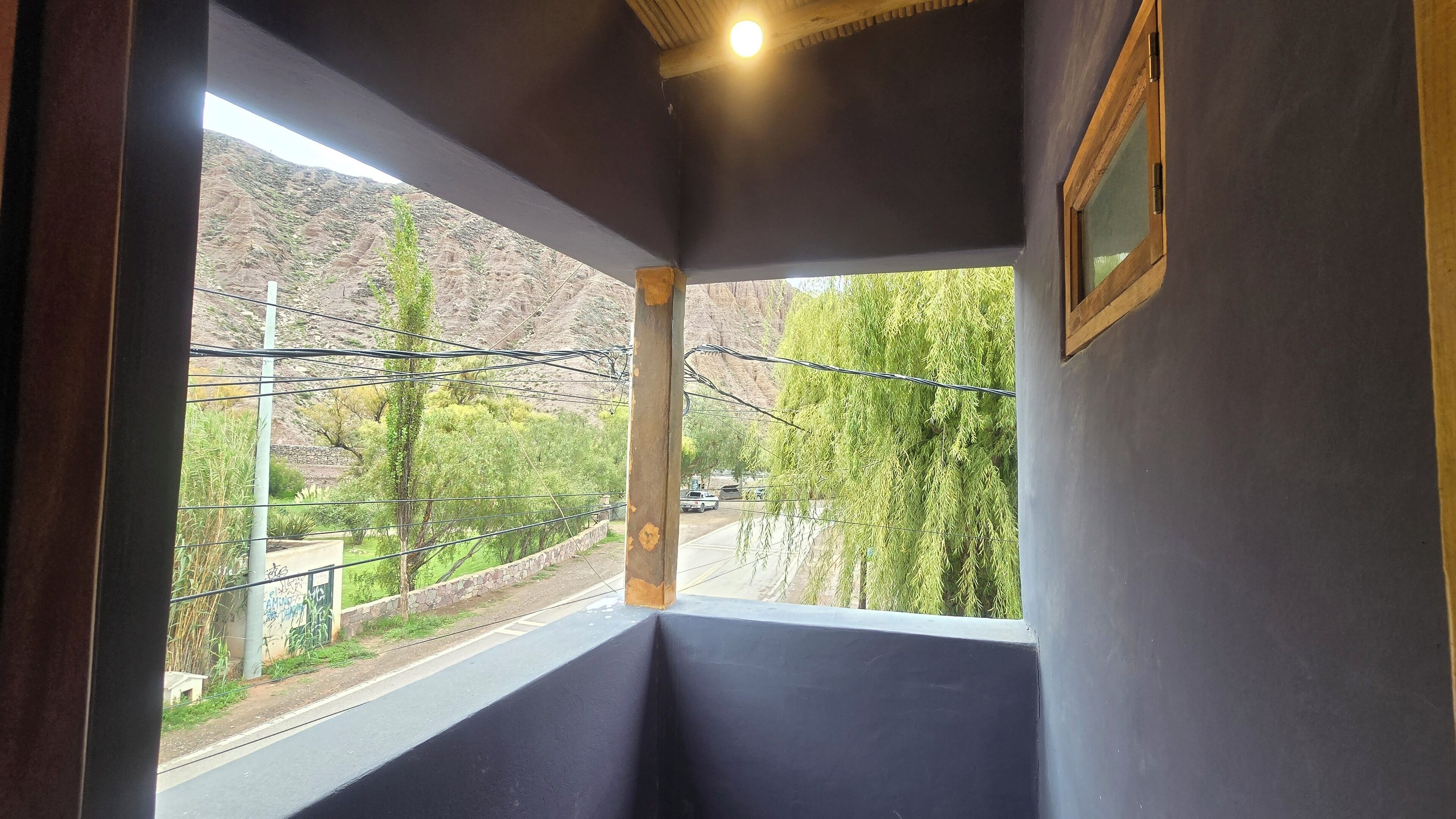A room with a window overlooking a road and a hilly landscape.