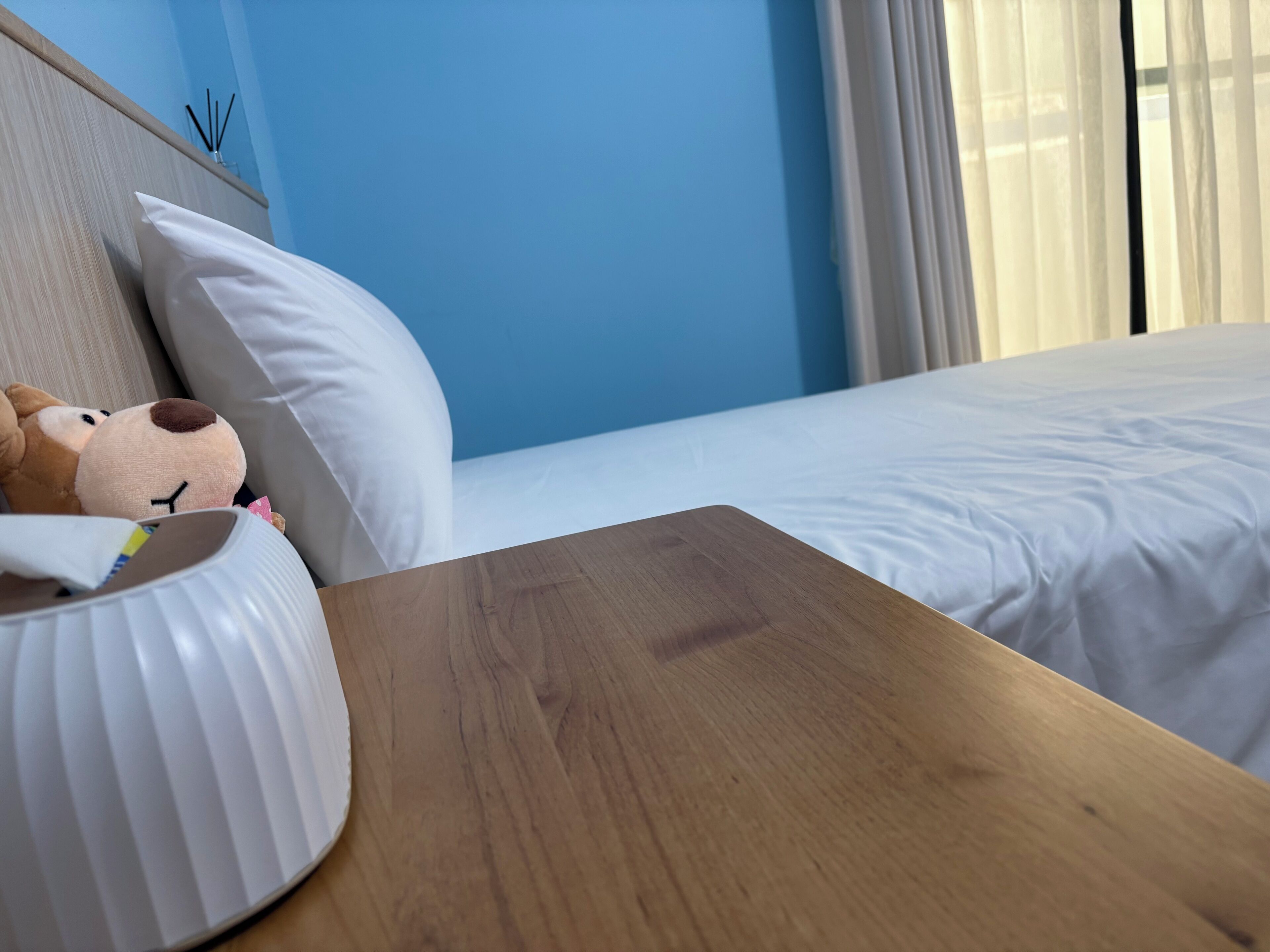 A hotel room with a wooden nightstand, a white pillow, and a plush toy.