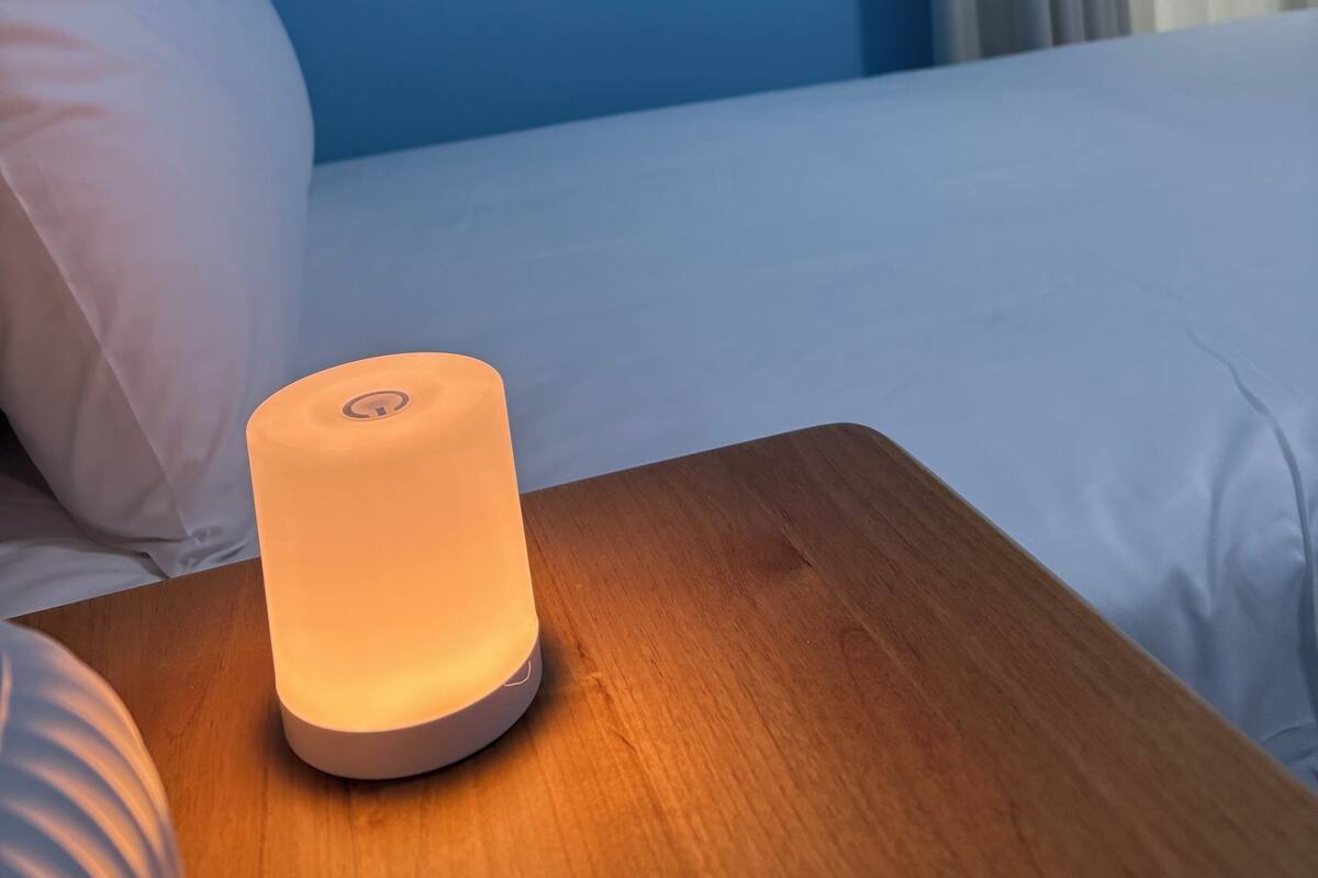 A bedside table with a white lamp, a bed with white bedding, and a blue wall.