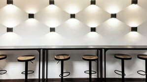 A bar area with hexagonal wall lights and wooden stools.