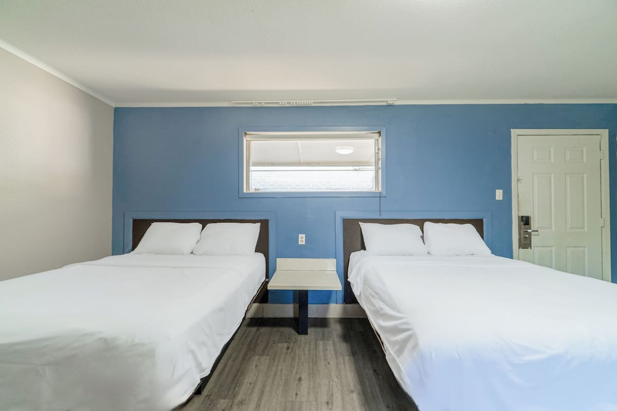A room with two single beds, a small table, a window, and a door.