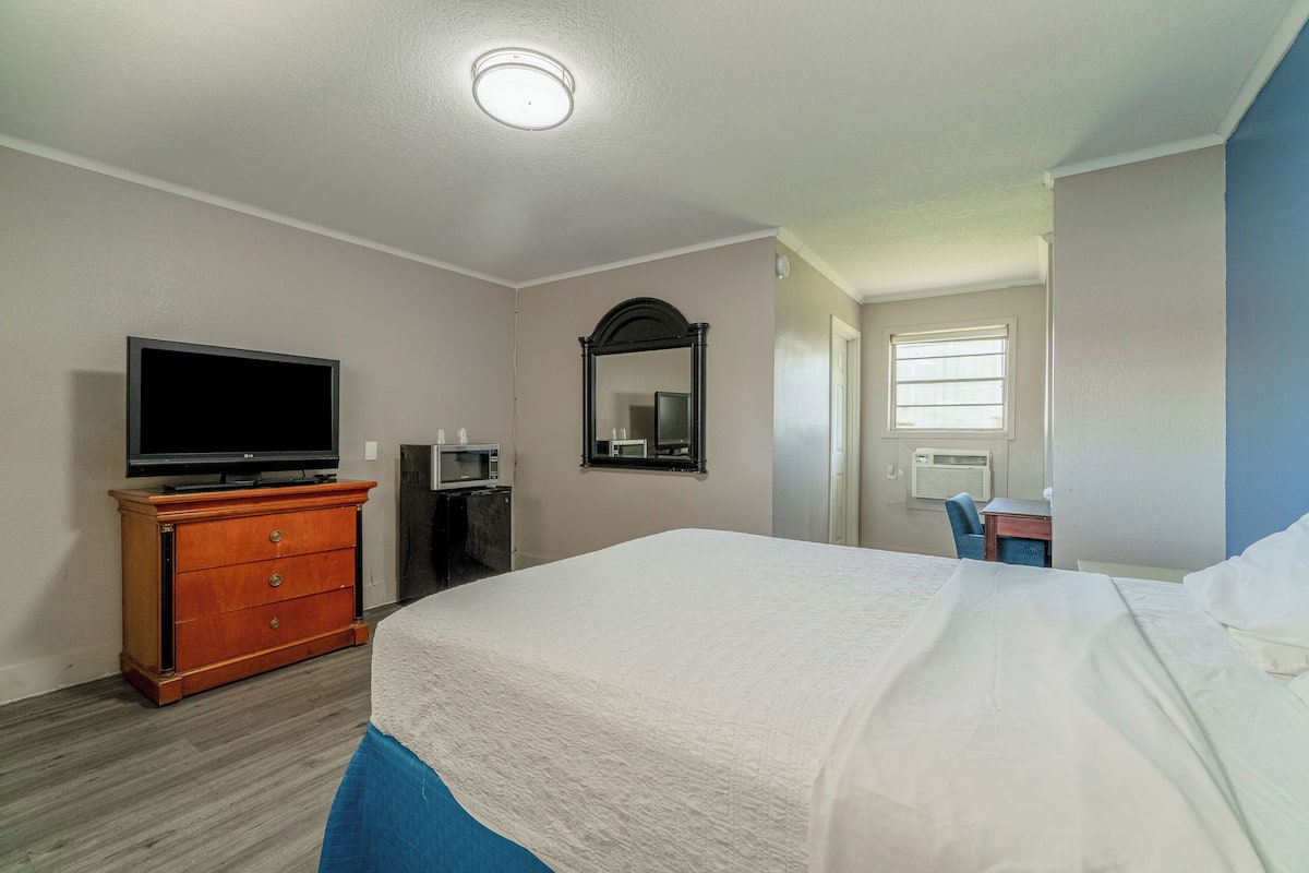 A hotel room with a bed, a dresser, a television, a mirror, and a desk with a chair.