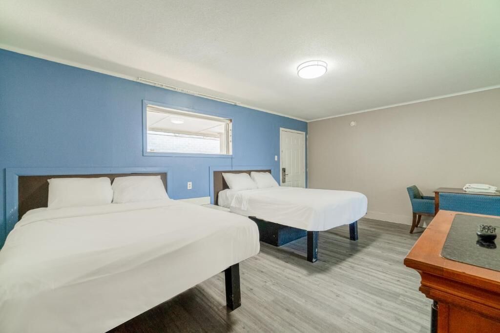 A hotel room with two beds, a desk, a chair, and a window.