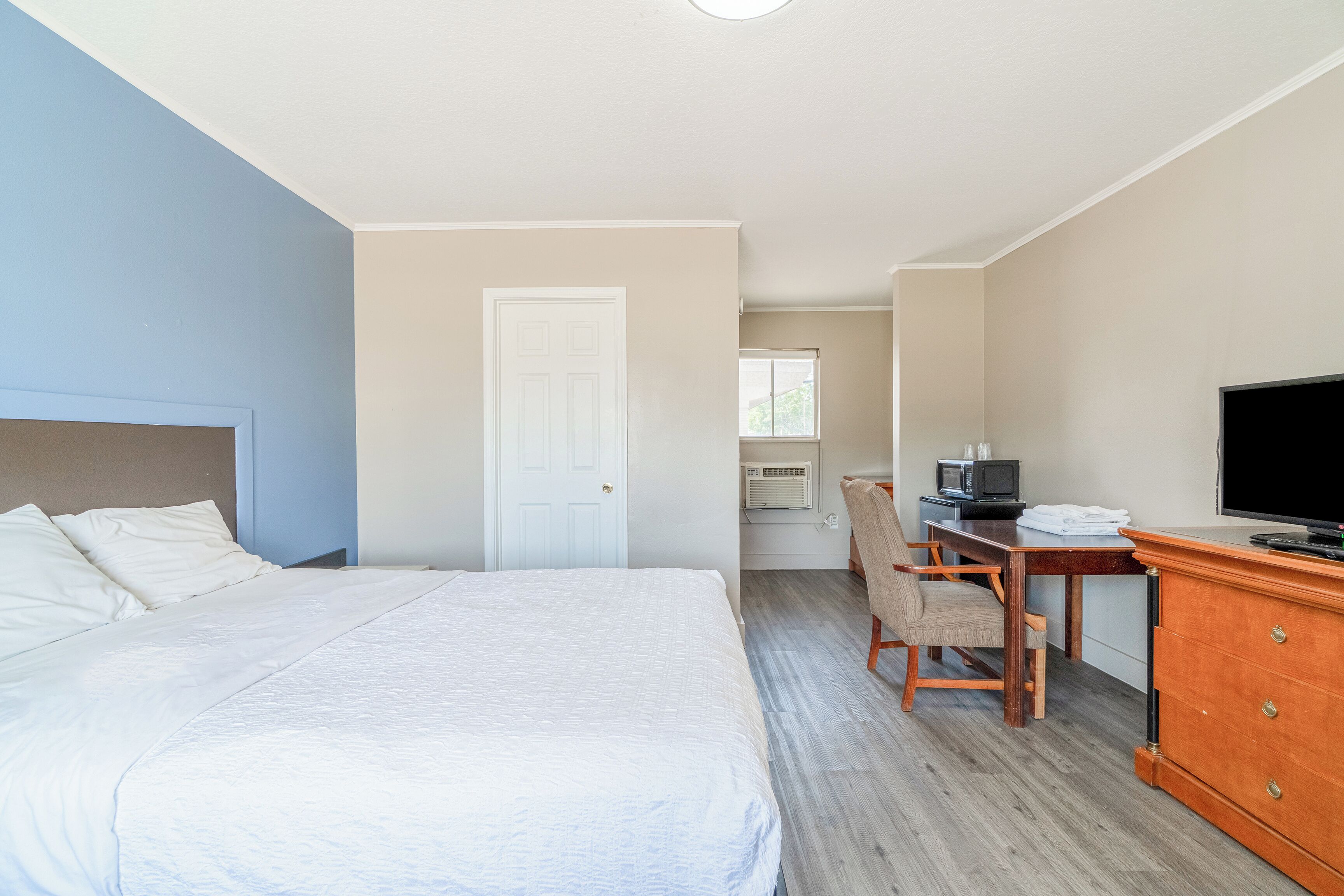 Una habitación de hotel con una cama, un escritorio con una silla, un televisor y un aparador.