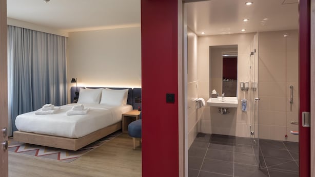 Une chambre d’hôtel moderne dotée d’un grand lit, d’une table de chevet et d’une salle de bain séparée avec douche et lavabo.
