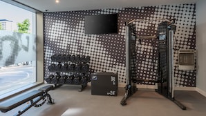 Une salle de sport équipée d’un téléviseur fixé au mur, d’un banc, d’haltères, d’un support à squats et d’un distributeur d’eau.