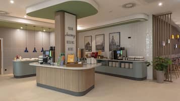 Un espace d’accueil moderne avec un comptoir central, une enseigne indiquant « VOTRE VOYAGE COMMENCE ICI » et une machine à café.