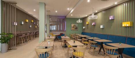 Un interior de restaurante moderno con mesas y sillas de madera, paredes verdes e iluminación decorativa.